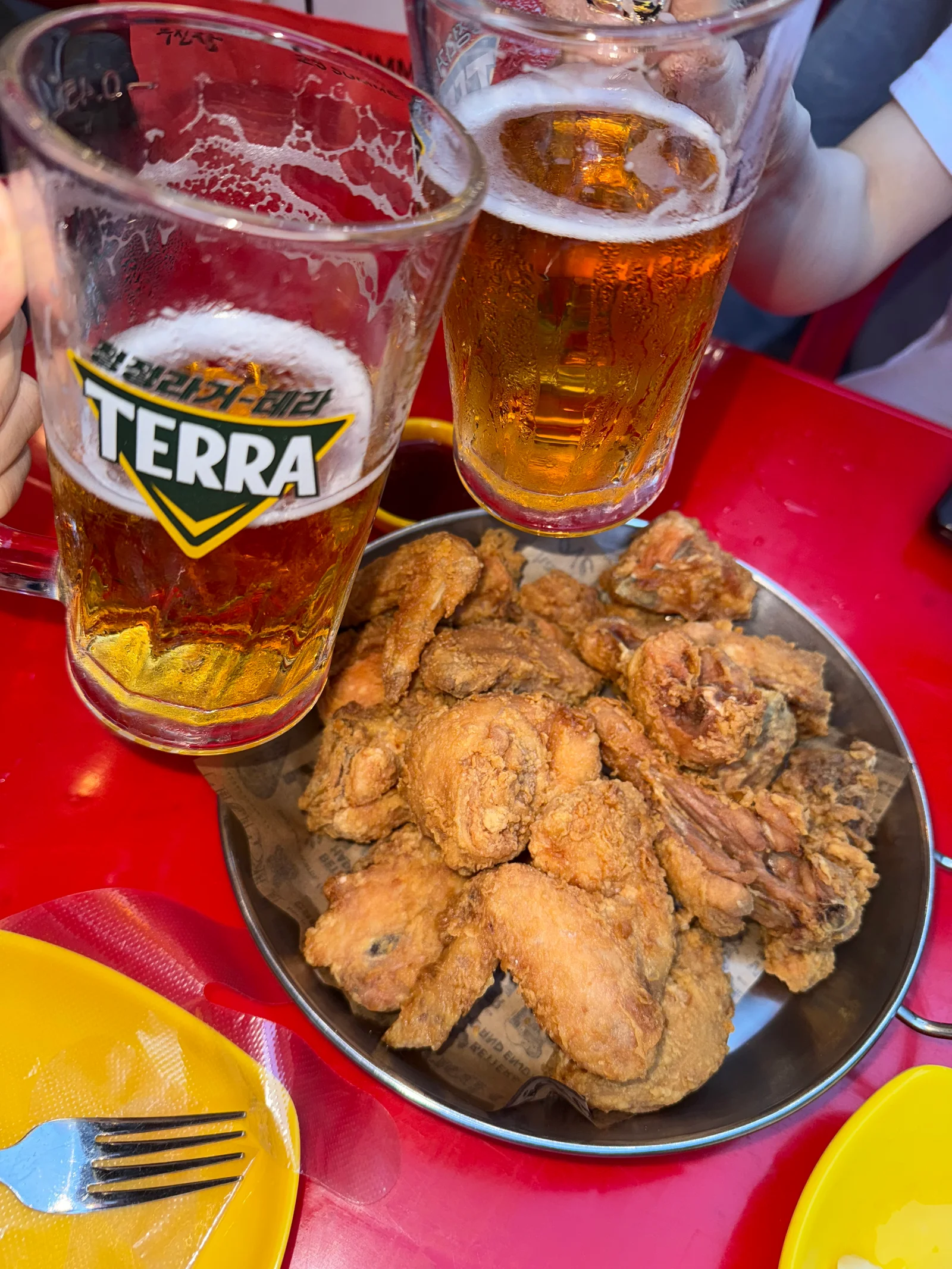 Two frosty mugs of Terra beer clinking over a platter of golden Korean fried chicken at BHC Myeongdong in Seoul